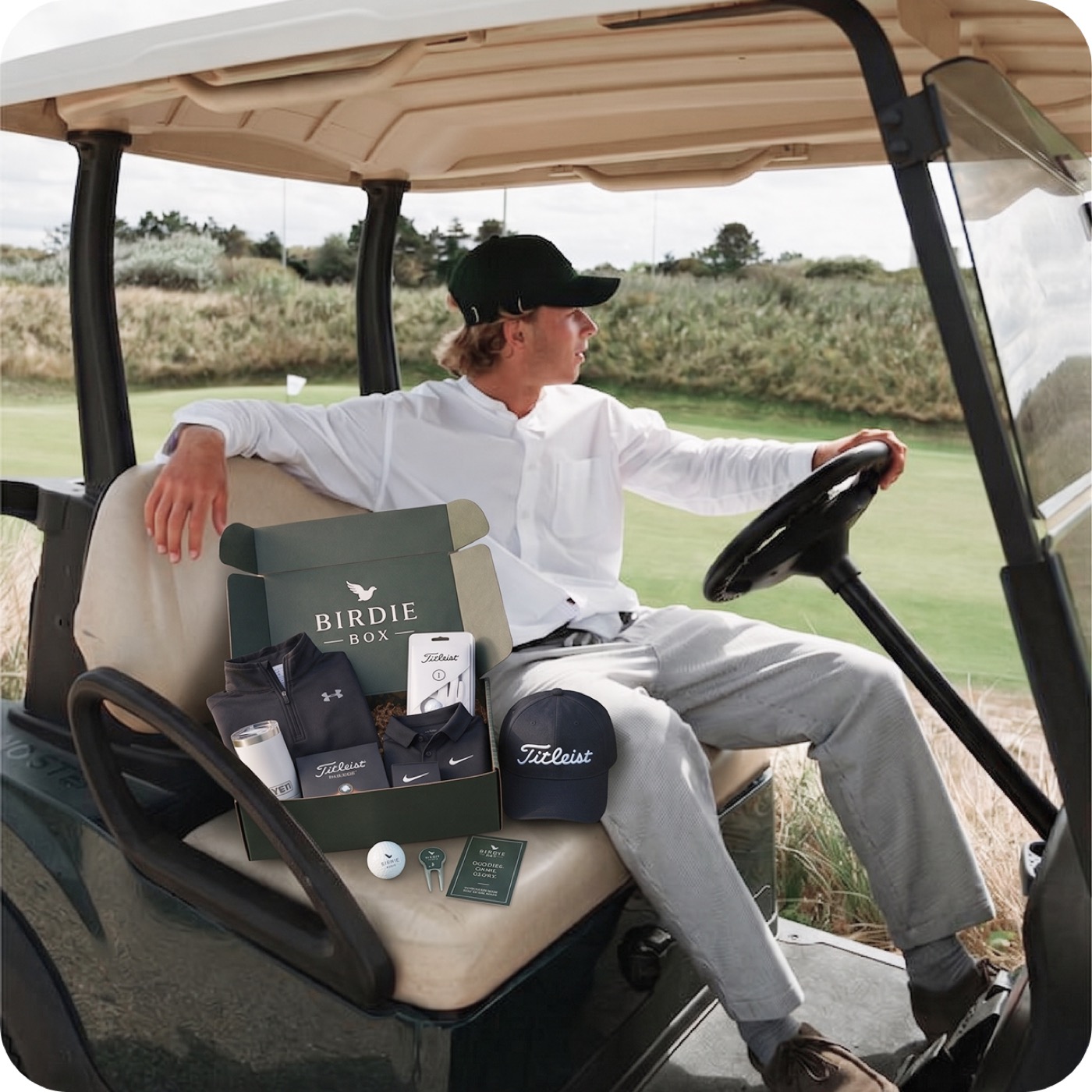 Golfer in a buggy with an open Birdie Box, Titleist balls and Nike cap